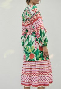 Rochie cu imprimeu floral, având frunze verzi, fructe roșii și portocalii, modele geometrice roz, mâneci lungi tip puff și talie subliniată cu un brâu.