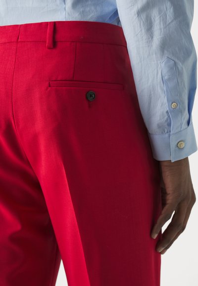 Røde skræddersyede bukser med en glat overflade, der har en baglomme med en sort knap og en slim fit. Iført en lyseblå skjorte.