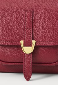 Red textured leather bag with a gold-tone clasp. Features a structured shape and stitching detail along the edges. Compact design.