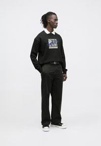 Sudadera negra con estampado gráfico, corte holgado, combinada con pantalones oscuros y zapatillas negras con suelas blancas. Diseño sencillo, detalles mínimos.