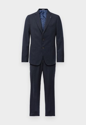 Costume bleu marine à rayures avec blazer à deux boutons, col cranté, poches à rabat et pantalon droit assorti sur fond blanc.