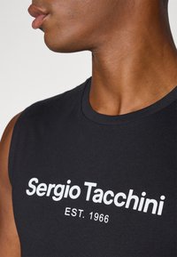 Černá bezrukávová košile vyrobená z bavlny, na přední straně s bílým textem "Sergio Tacchini EST. 1966". Hladká textura, minimalistický design.