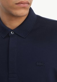 Navy polo shirt made of textured fabric, featuring a three-button placket, a ribbed collar, and an embroidered logo on the chest.