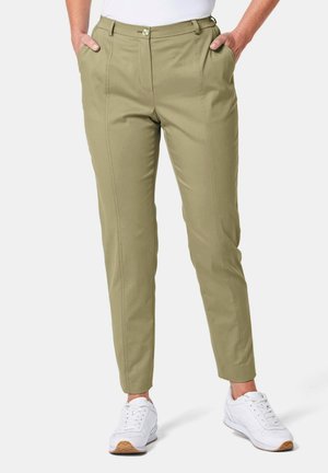 Hellolivgrüne, taillierte Hose mit zwei vorderen Taschen und einem Reißverschluss, die durch klare Linien und eine glatte Textur besticht, kombiniert mit weißen Sneakers.