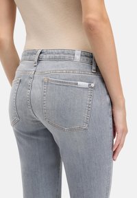 Jasnoszare dżinsy z denimu o dopasowanym kroju, z wysokim stanem, wieloma kieszeniami i subtelnymi detalami przeszyć.