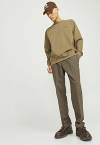 Olivgrön sweatshirt med muddade ärmar, kombinerad med ljusbruna veckade byxor. Brunt cap och mörkbruna skor med tofsar.