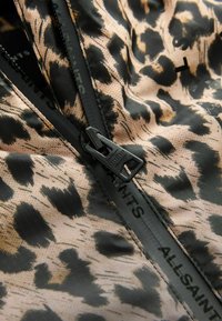 Leopardenmusterstoff mit schwarzen Akzenten, ausgestattet mit einem schwarzen Reißverschluss und der 'ALLSAINTS'-Markierung entlang der Naht. Strukturmaterial, leicht.