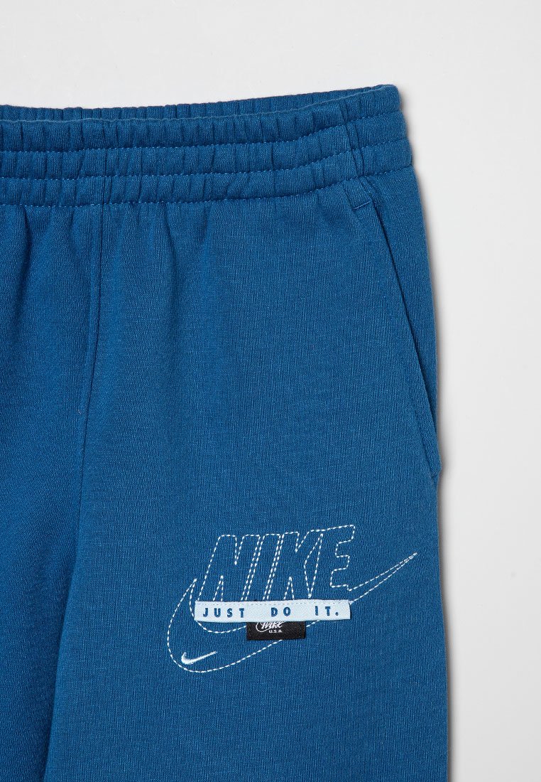 Pantalones de chándal de algodón azul con cintura elástica, bolsillos laterales y un logo de "Nike" bordado en blanco en la pierna izquierda.