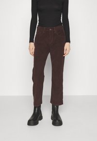 Pantalones de pana marrón con corte recto, con cierre frontal de botón y bolsillos laterales, combinados con botas negras hasta el tobillo.