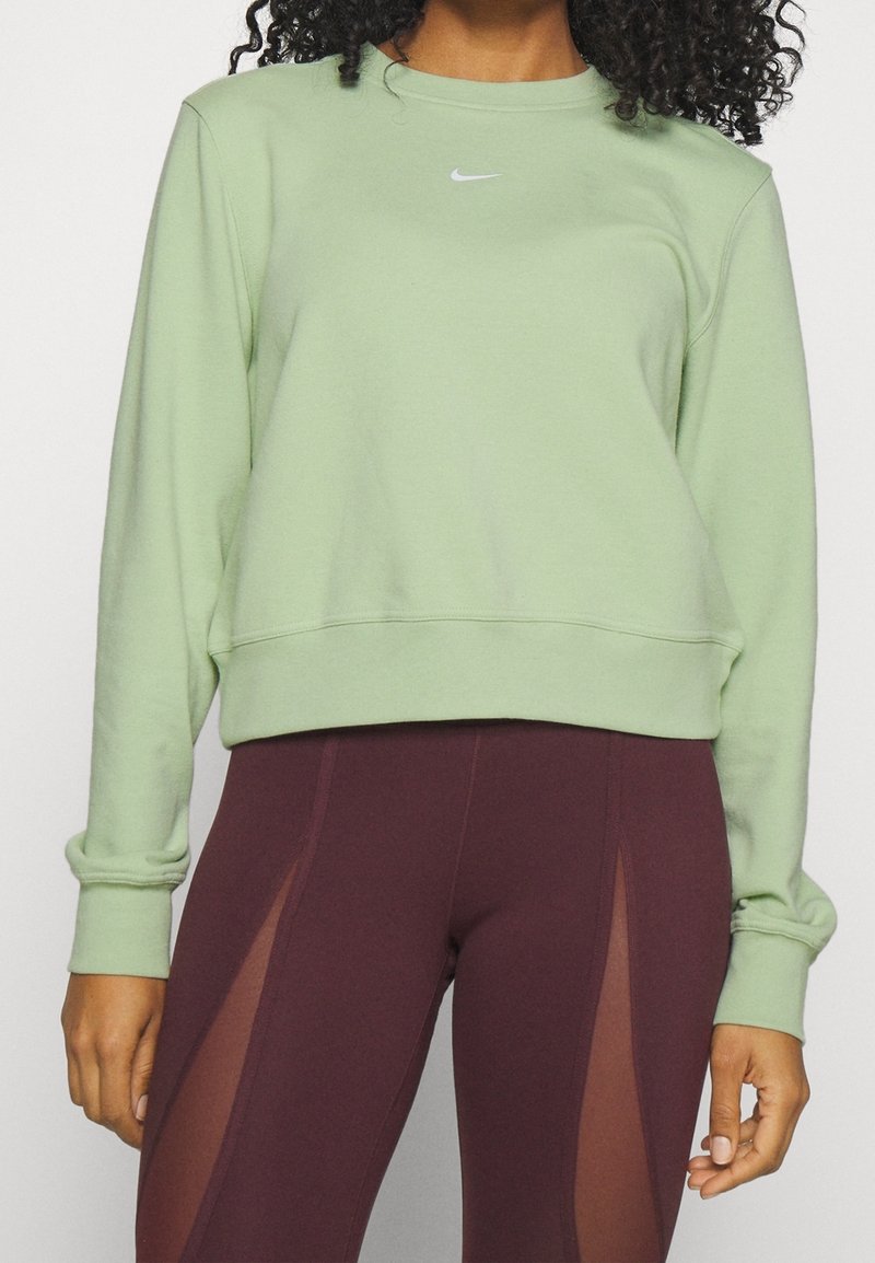 Sudadera verde claro con cuello redondo y mangas con puños, que presenta un pequeño logo blanco en el pecho. Combinada con leggins burdeos.