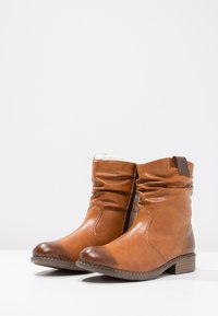 Bottines en cuir marron avec un design froncé, bout rond et un petit talon bloc. Présente des coutures contrastées et une fermeture éclair sur le côté.