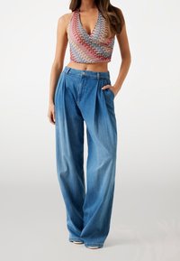 Farverig mønstret halterneck crop top med plisserede lyseblå vide jeans. Den denim har en knaplukning og sidelommer.