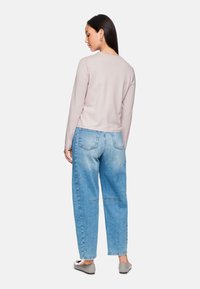 Helles rosa Langarmoberteil kombiniert mit hochtaillierten hellblauen Jeans. Die Jeans haben eine lockere Passform und vordere Taschen. Graue Ballerinas sind sichtbar.