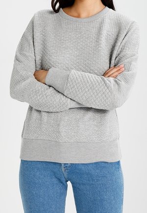Felpa grigia trapuntata con collo rotondo e polsini a costine, caratterizzata da una finitura testurizzata e una vestibilità rilassata. Abbinata a jeans blu.