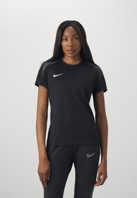 Must küllastunud sportlik t-särk lühikeste varrukatega ja ümmarguse kaelusega. Rinnal on valge Nike logo, millele on lisatud tumedad sportlikud püksid.