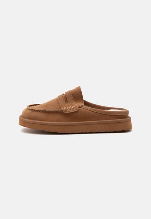 Mule mocassin marron en daim sans talon avec des détails cousus et une semelle en caoutchouc, conçue pour une utilisation intérieure et décontractée.
