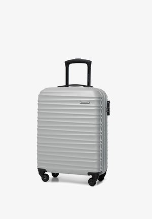 Silver hard-shell suitcase with textured ridges, black retractable handle, and four spinner wheels. Durable design with logo detail.