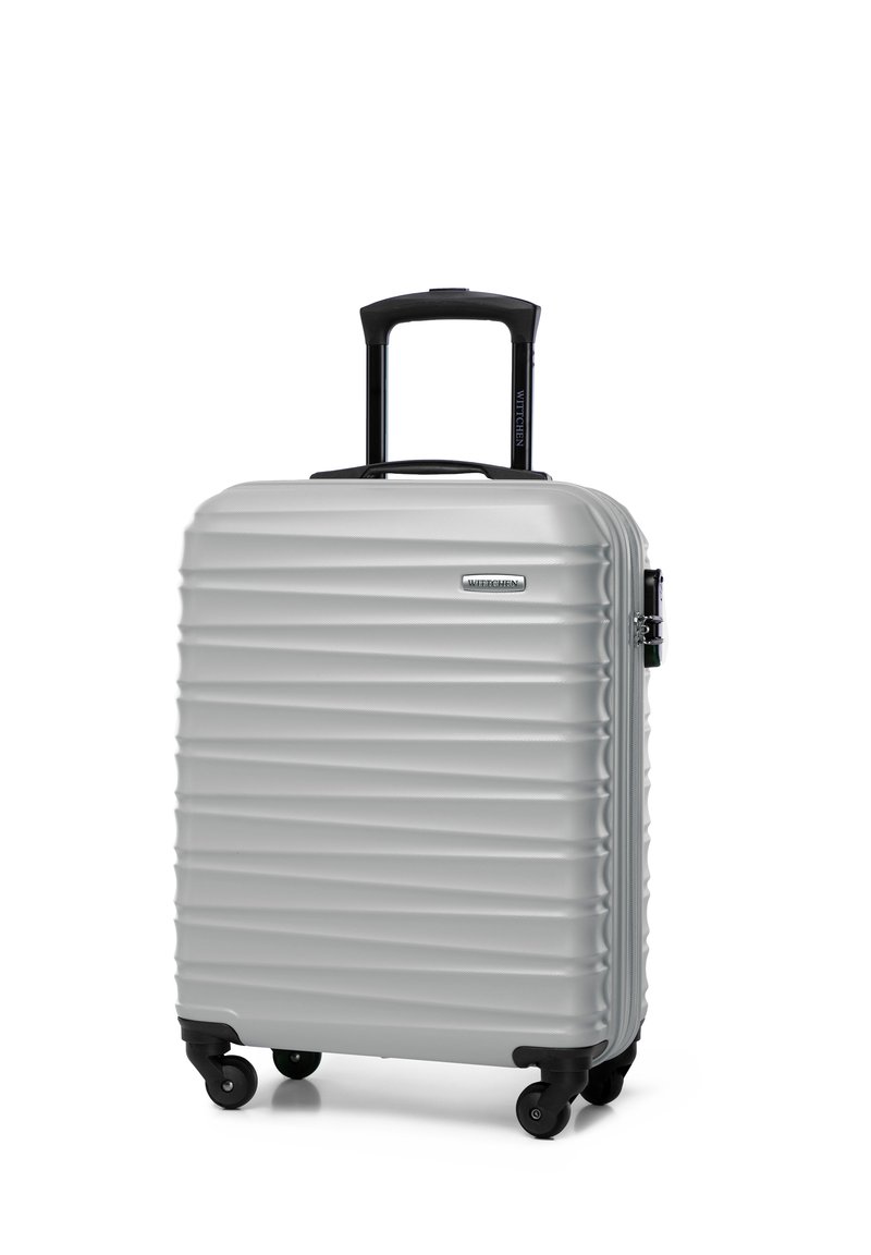 Silver hard-shell suitcase with textured ridges, black retractable handle, and four spinner wheels. Durable design with logo detail.