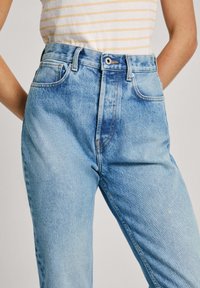 Jeans de talle alto en azul claro con un ligero desgaste, que cuentan con un diseño tradicional de cinco bolsillos y costuras de contraste sutiles.