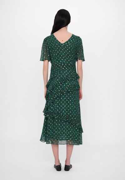 Zelené květinové šaty s výstřihem do V, krátkými rukávy, vrstvenými volánky a midi délkou. Vyrobené z lehké, průsvitné látky. Černé boty.