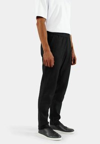 Svart, elastisk midjebåndbukse laget av vevd stoff; rett snitt med sidesømmer; brukt med svarte joggesko og en hvit kortermet skjorte.