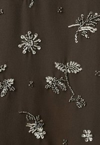 Tissu foncé brodé de petits motifs floraux en perles argentées dispersés sur la surface en formes et tailles variées.