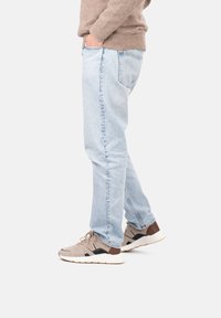 Jeans dritti azzurri chiaro, un maglione lavorato beige e scarpe da ginnastica beige con accenti neri e suola bianca, viste di lato.
