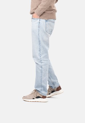 Un jean bleu clair à jambe droite, un pull en laine beige et des chaussures de sport beiges avec des accents noirs et une semelle blanche, vues de côté.