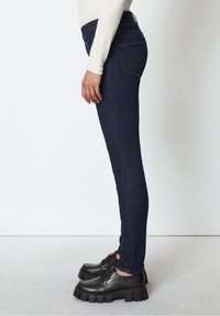 Skinny dark denim jeans with a smooth texture, high waist, and two back pockets. Paired with chunky black lace-up shoes.
