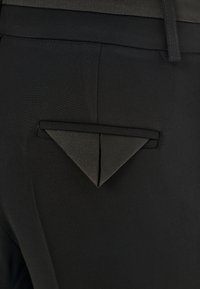 Pantaloni neri con una vestibilità su misura e un dettaglio a tasca triangolare. Il tessuto è liscio, con linee pulite e una trama sottile.