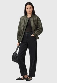 Oliven grøn quiltet bomberjakke med ribbede manchetter, parret med sorte højtaljede jeans og flade sorte sko. Holder en lille sort taske.