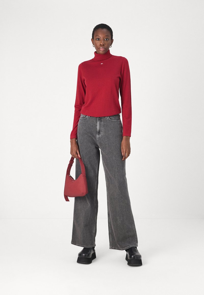 Roter Rollkragenpullover, graue Marlenehosen, schwarze Plateausch Schuhe und eine rote Handtasche. Glatte Texturen, lässiges Design und stimmiges Farbschema.