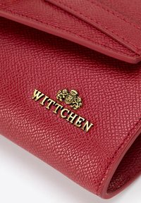 Portafoglio in pelle rossa con texture, caratterizzato da un logo "WITTCHEN" in tonalità oro e da un emblema decorativo di leone, con bordi cuciti e chiusura a pattina.