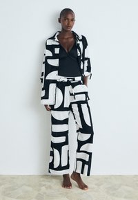 Conjunto de loungewear con estampado en blanco y negro que incluye una camisa de botones y pantalones de pierna ancha, hecho de tejido ligero y con un corte relajado.