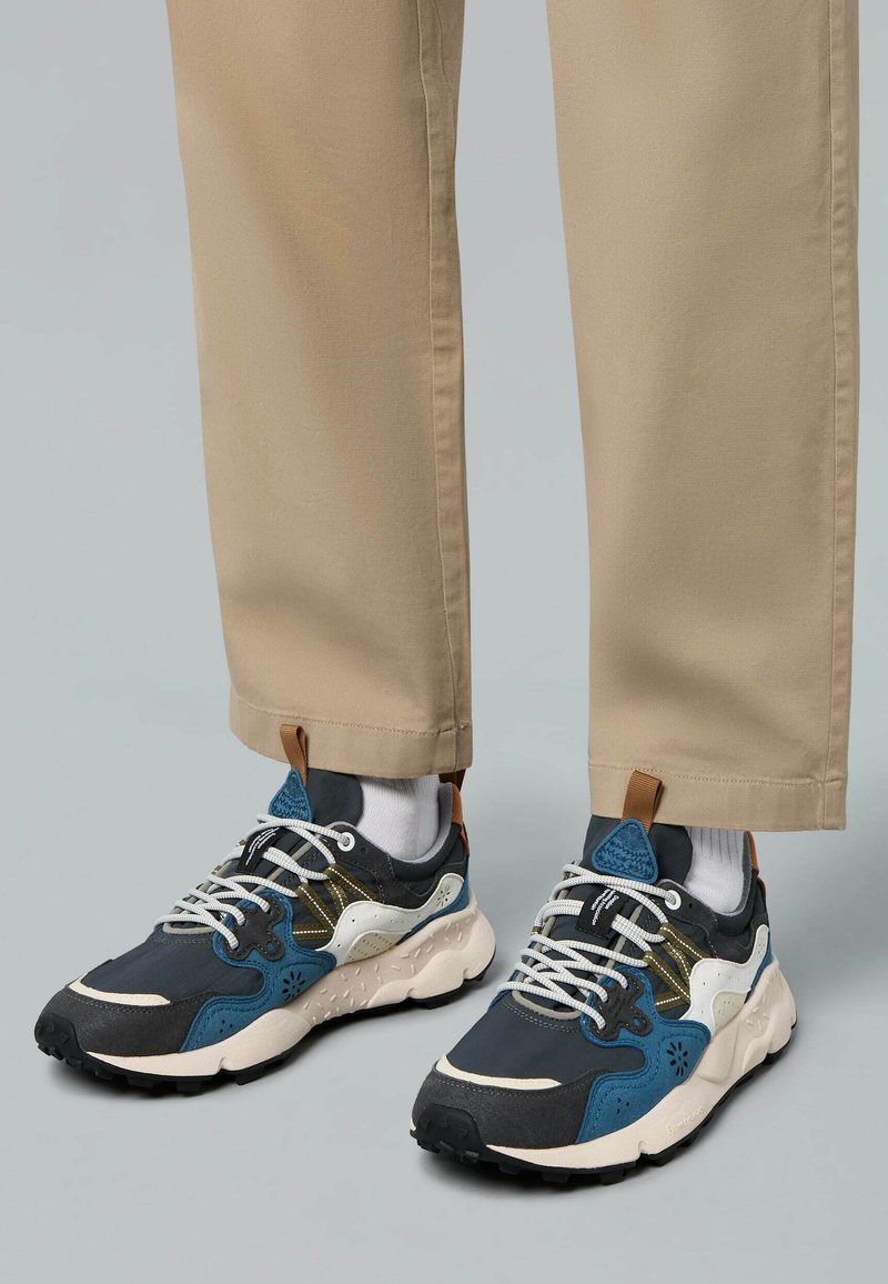 Sportliche Schuhe mit einer Mischung aus dunkelgrauem, blauen und cremefarbenen Materialien. Strukturiertes Obermaterial mit weißen Schnürsenkeln und schwarzem Gummi-Außensohle.