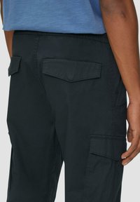 Zwarte cargobroek van katoen, met een koord in de taille, twee achterzakken en zijzakken met klep sluitingen.