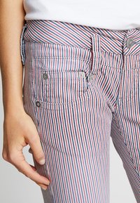 Randiga byxor med vertikala linjer i röd, vit och blå, med en åtsittande midja, framfickor och metalldetaljer.