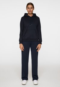 Felpa blu navy con pantaloni coordinati a taglio morbido. La felpa presenta una tasca a marsupio e un cordoncino, abbinata a sneaker bianche.