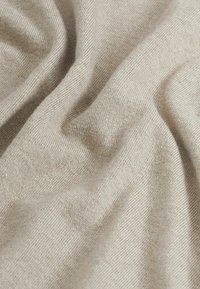 Tessuto di lana beige morbido con una fine trama a maglia e pieghe delicate che creano ombre e riflessi sottili.