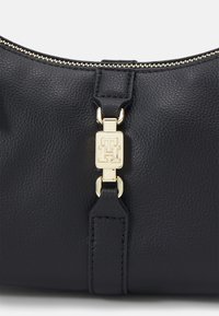 Černá kožená kabelka s texturovaným povrchem, vybavená zlatými kovovými prvky a logem značky na obdélníkovém detaile.