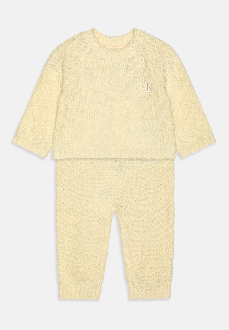 Gelbes gestricktes zweiteiliges Outfit mit einem langärmeligen Oberteil mit Rundhalsausschnitt und zwei Knöpfen sowie passenden Hosen mit elastischen Bündchen.