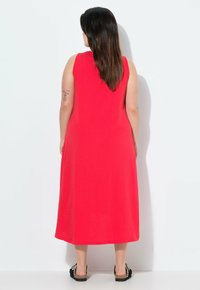 Abito midi rosso senza maniche con scollo rotondo e texture morbida. Presenta una vestibilità rilassata, che scende sotto il ginocchio. Indossato con sandali neri.