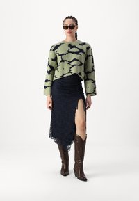 Πράσινο και μαύρο πουλόβερ με μοτίβο, ναυτικών χρωμάτων φούστα δαντέλας με άνοιγμα στο πλάι, καφέ καουμπόικες μπότες με πολύπλοκες λεπτομέρειες.