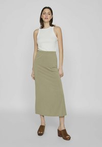 Falda maxi elástica de color verde oliva con una cinturilla elástica; combinada con una camiseta sin mangas ajustada de canalé blanca y zapatos de plataforma marrones.