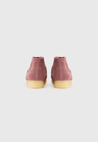 Botas de tornozelo em camurça rosa com biqueira arredondada e textura suave, apresentando uma sola de borracha de cor clara e detalhes cosidos.