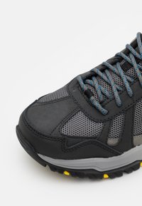 Černá a šedá sportovní bota s svrchní částí z síťoviny a nubuku, kulatá špička, šedá gumová podešev a modré tkaničky. Žluté akcenty na podrážce.