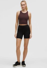 Tumši brūns crop top ar noapaļotu apkakli. Melni šorti ar augstu jostasvietu. Modelis valkā melnus sporta apavus. Gludas tekstūras.