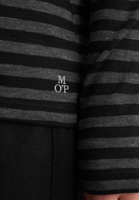 Svart og gråstripet langermet skjorte med en liten hvit logo "M O'P" på nederste kant. Myk strikket tekstur med figursydd design.