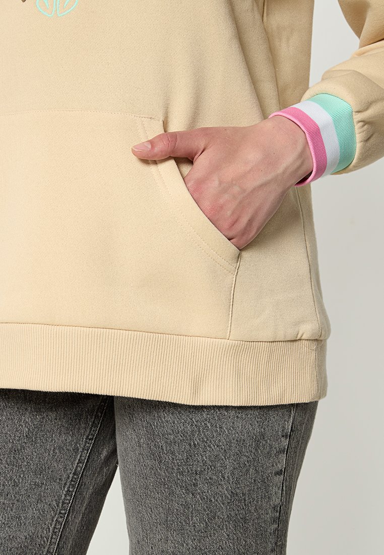 Beżowy sweter z przednią kieszenią, żebrowym dołem i mankietami z miętowo-zielonymi, różowymi i białymi paskami. Miękka tkanina o gładkiej teksturze.