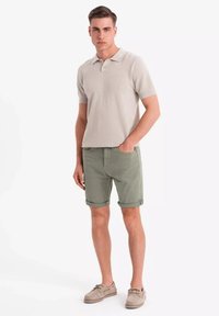 Polo shirt gris clair à manches courtes, associé à un short vert retroussé et des chaussures beiges. Le tissu semble texturé et ajusté.